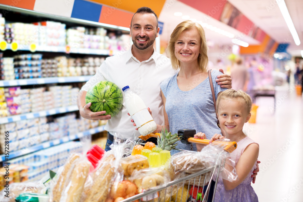 Happy family standing with full cart in supermarket