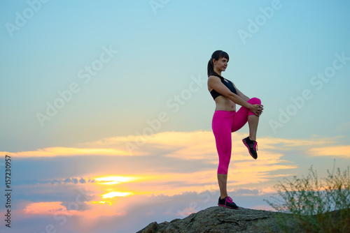 Young Fitness Woman Stretching on the Top of Rock. Female Runner Doing Stretches . Healthy Lifestyle Concept.