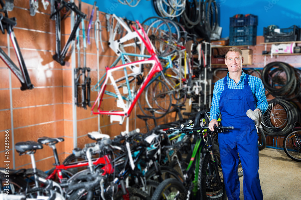 Obraz premium Positive man seller in uniform holding bicycle