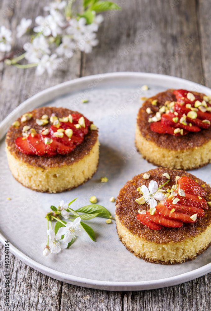 Pieces of homemade semolina cake with strawberry and pistachio decorated flowers of cherry on a rustic vintage wooden table. Selective focus Pieces of homemade semolina cake with strawberry and pistachio decorated flowers of cherry on a rustic vintage wooden table. Selective focus