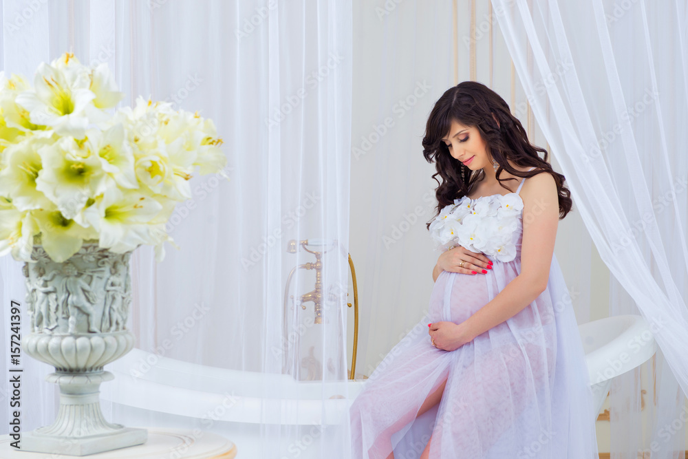 Gentle pregnancy. Beautiful pregnant in light white dress with orchids Gentle pregnancy. Beautiful pregnant in light white dress with orchids