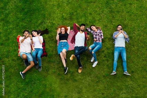  Group of young people laying on the grass, using phones