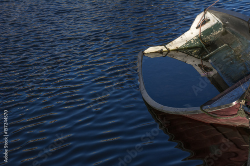 Old boat with some water inside it is on the river in the day