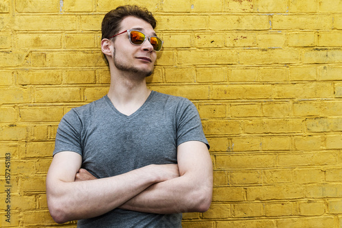 Photos Pretty handsome confident young man hipster with sunglasses smiling behind yellow wall