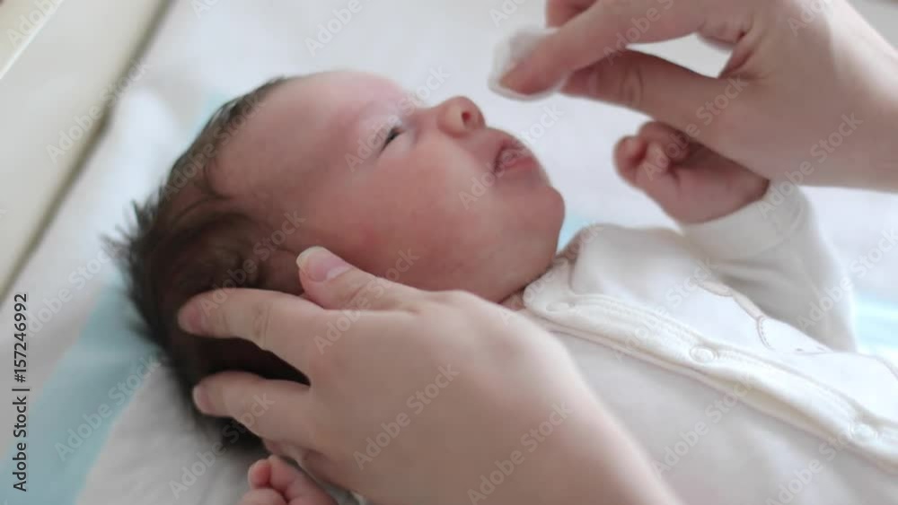 Mother is wiping a baby face with a cotton pad (close-up) Mother is wiping a baby face with a cotton pad (close-up)