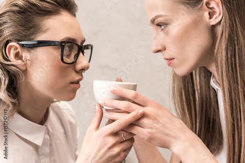 Side view of beautiful young women holding coffee cup and looking at each other