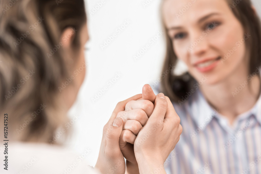 close up of young smiling girlfriends sitting and holding hands close up of young smiling girlfriends sitting and holding hands