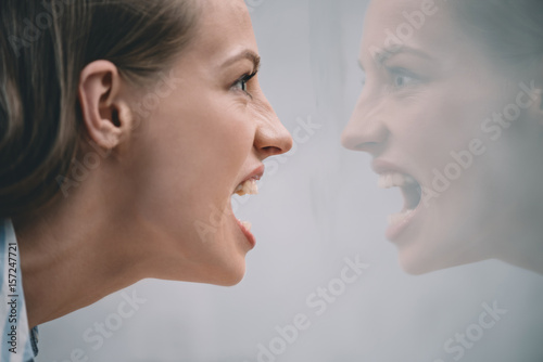 aggressive stressed woman screaming at her reflection in mirror
