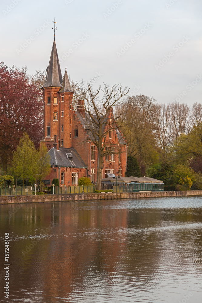 Minnewater gothic castle is reflected in Lake of Love at quiet spring evening in the light of sunset, Bruges (Brugge), Belgium