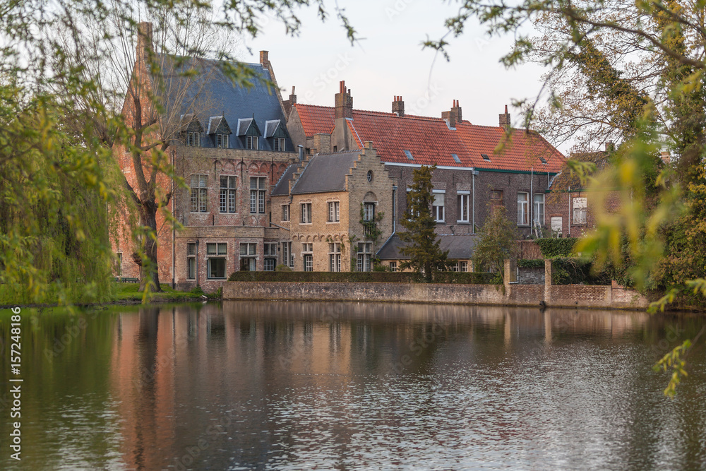 The medieval neighborhood at the Begijnhof with brick buildings over lake of Love in Minnewater park in the light of sunset, Bruges (Brugge), Belgium