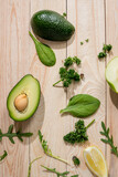Top view of sliced avocado and fresh raw greens on wooden background
