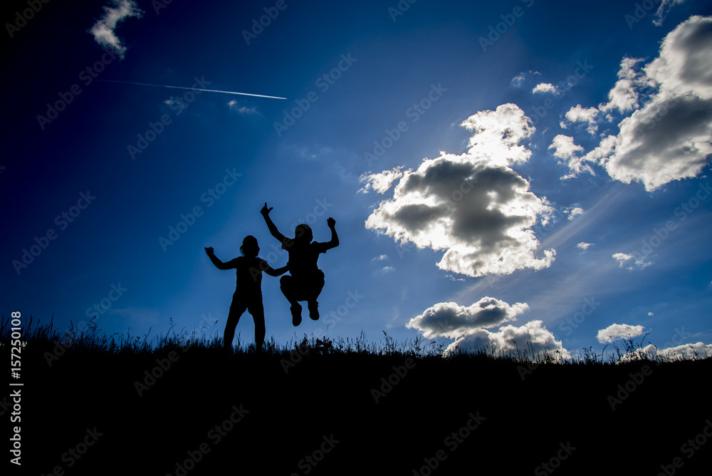 The silhouettes of two children on the top one hill and the clear sky with some clouds