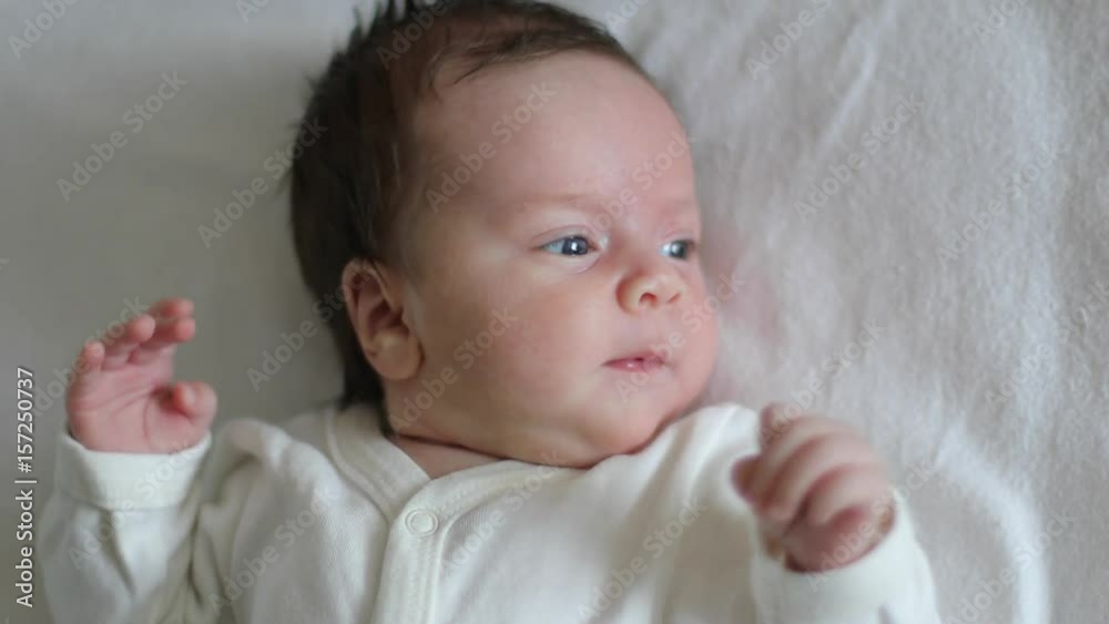 Newborn baby is lies in a cot, looking around and waving his arms (close-up)