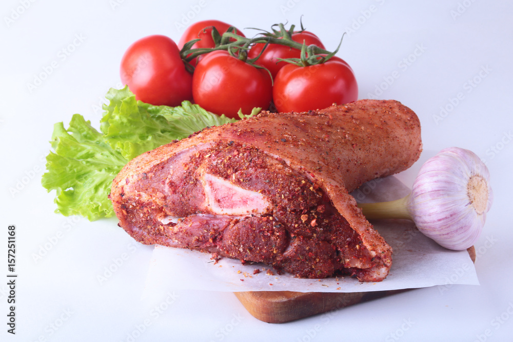 Raw pork knuckle and vegetables, garlic, tomatoes spices and lettuce leaves on a cutting board. Selective focus. Ready for cooking. Raw pork knuckle and vegetables, garlic, tomatoes spices and lettuce leaves on a cutting board. Selective focus. Ready for cooking.