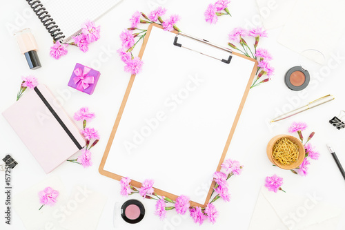 Blogger or freelancer workspace with clipboard, notebook, pink flowers and accessories on white background. Beauty blog concept. Flat lay, top view.