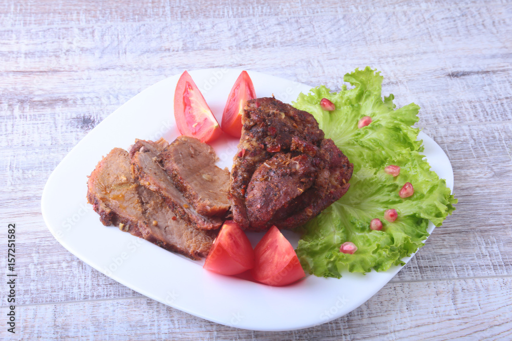 Steak of grilled meat with tomato, lettuce and beans pomegranate on white plate.