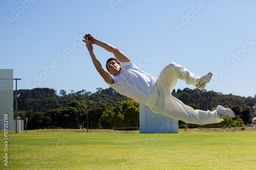 Full length of player diving to catch ball against blue sky