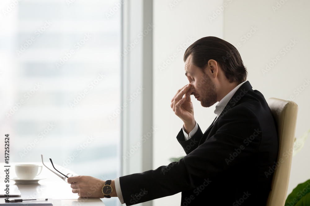 Φωτογραφία Tired businessman at desk holding eyeglasses in hand and massaging nose bridge