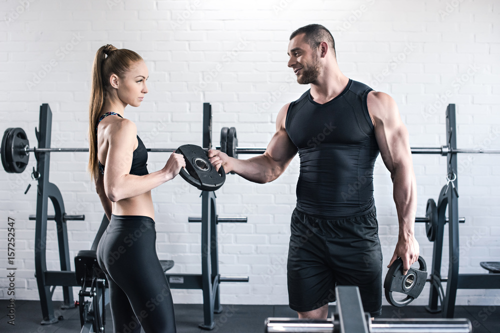Athletic man and woman in sportswear holding weights in gym Athletic man and woman in sportswear holding weights in gym