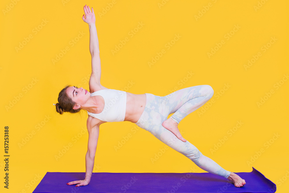 Naklejka premium Young yogini woman stretching on purple mat isolated on yellow background