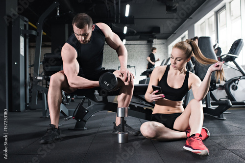 man training with dumbbell while woman using smartphone at gym