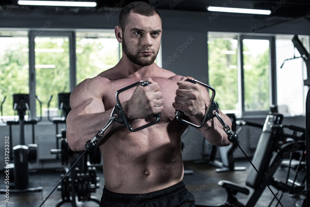 young shirtless bodybuilder training with weight machine at gym young shirtless bodybuilder training with weight machine at gym