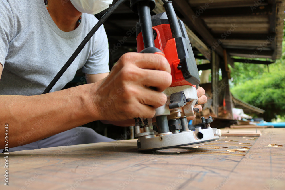 Asian workers using electric routering to cut down stripes on the wood.  