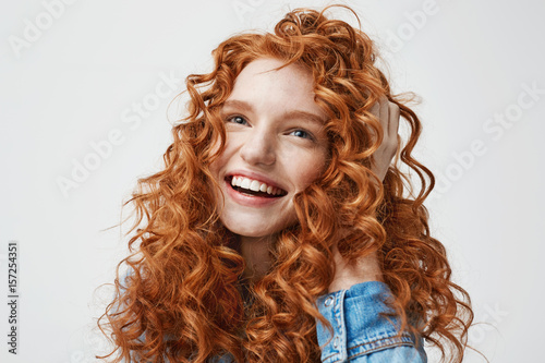 Portrait of cute happy girl smiling touching her curly red hair over white background.