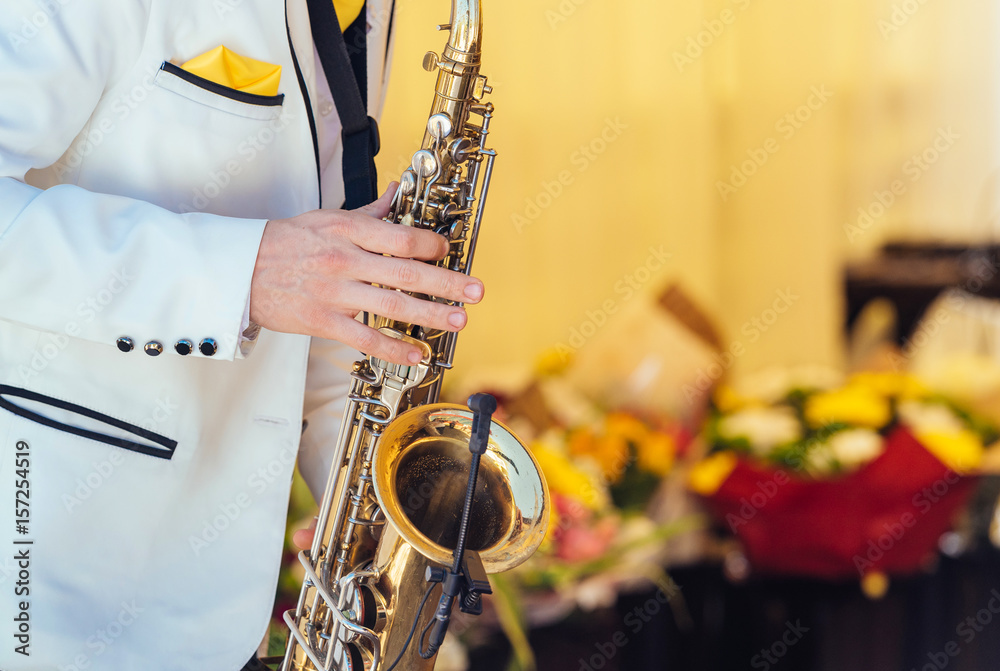Fototapeta premium Saxophonist in white jacket plays the saxophone. Saxophonist jazz man with saxophone on wedding party