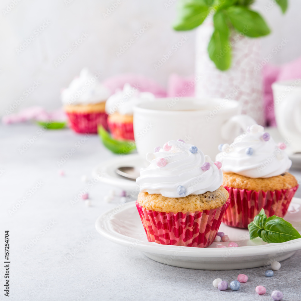 Mini cupcakes with white frosting cream and pink sprinkles on light gray background. Decorated with basil leaves. Party food concept. Copy space. Mini cupcakes with white frosting cream and pink sprinkles on light gray background. Decorated with basil leaves. Party food concept. Copy space.