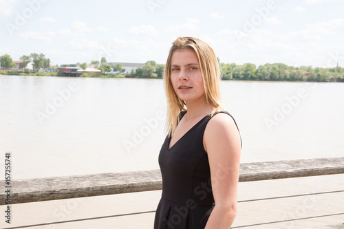 girl by the river in town with blond hair and a black dress © OceanProd