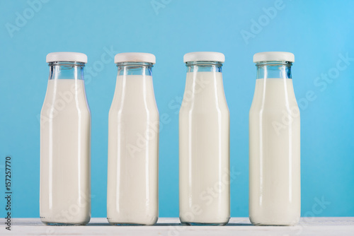 row of glass bottles with milk on tabletop at blue background