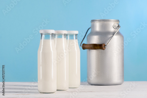 fresh milk in glass bottles and milk can near by on wooden tabletop