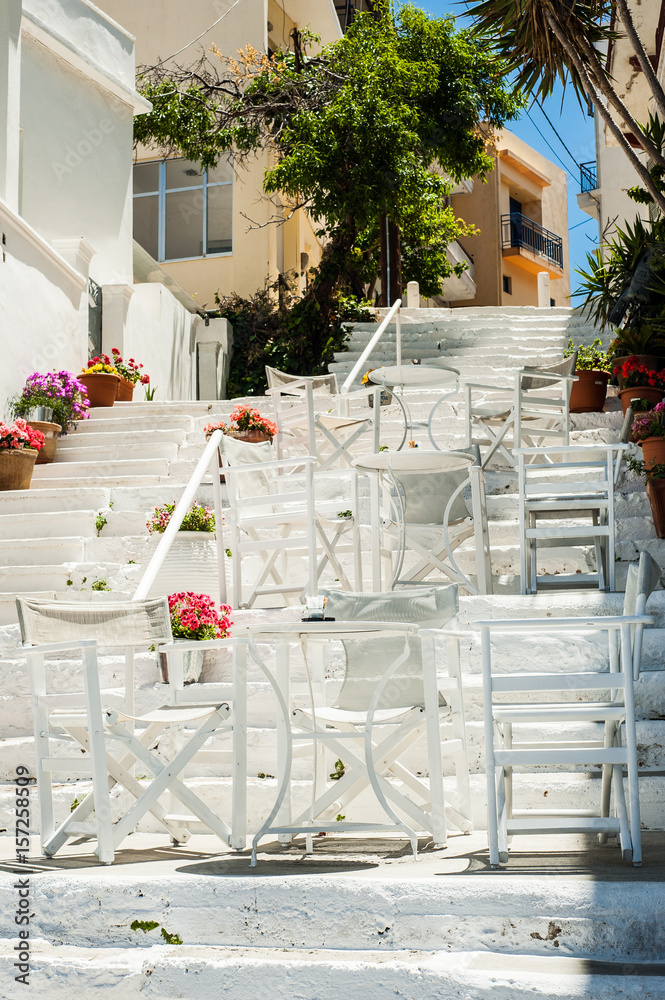 White Greek stairs with tables and chairs. Typical Greek street with flowers