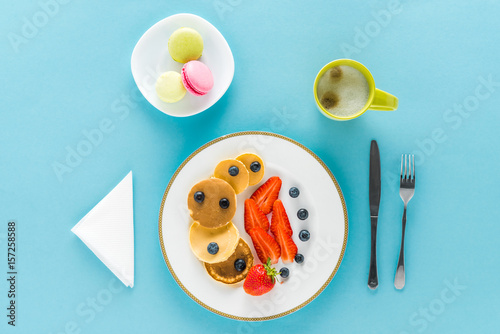 top view of pancakes with berries on plate with macarons on blue background