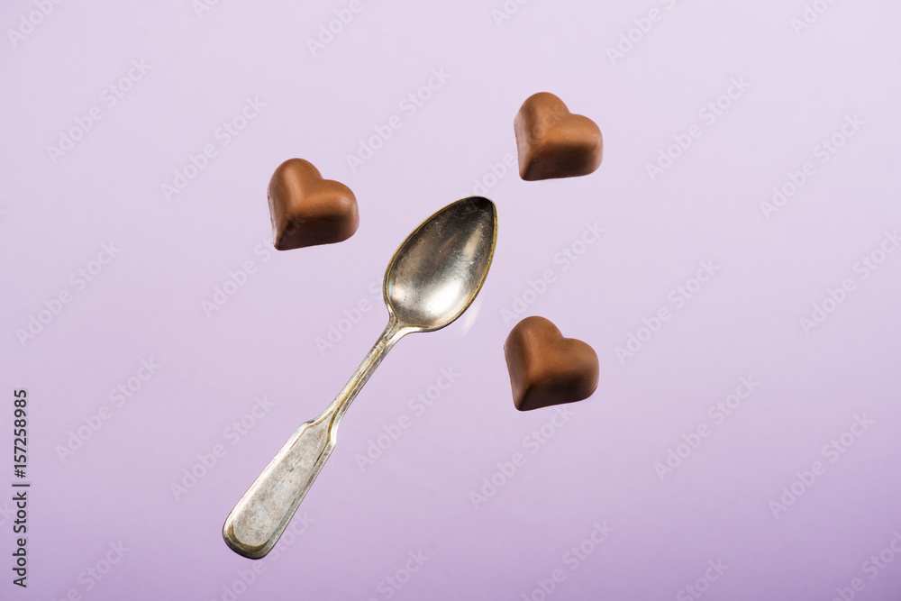 top view of heart shaped chocolate candies and spoon isolated on pink