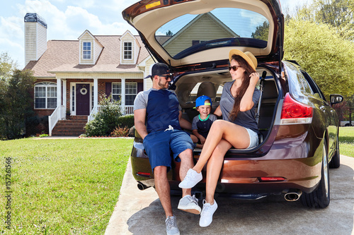 Family sits cars trunk near house. Mother, father, son. photo