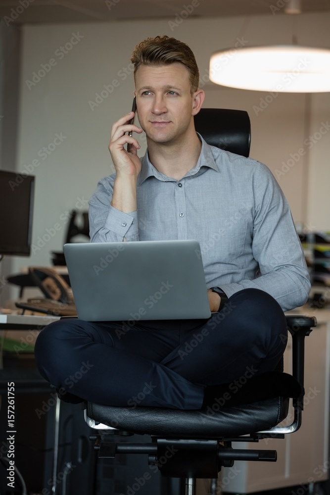 Executive talking on mobile phone while using laptop Executive talking on mobile phone while using laptop