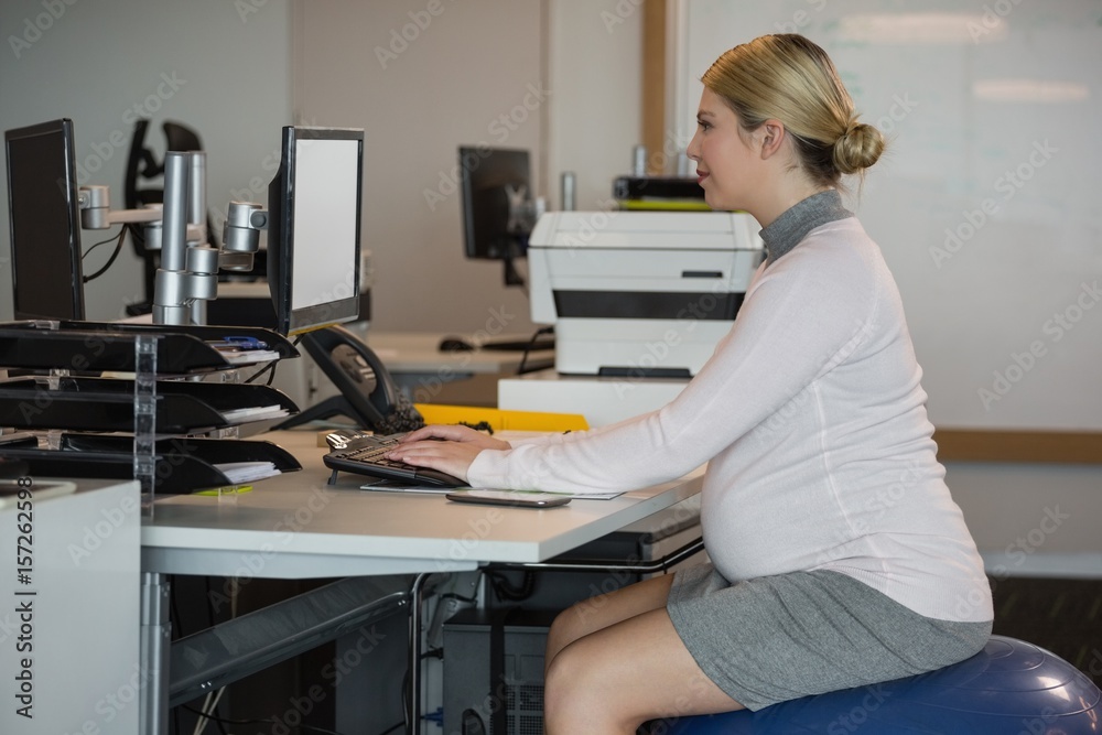 Pregnant woman sitting on fitness ball while working at desk