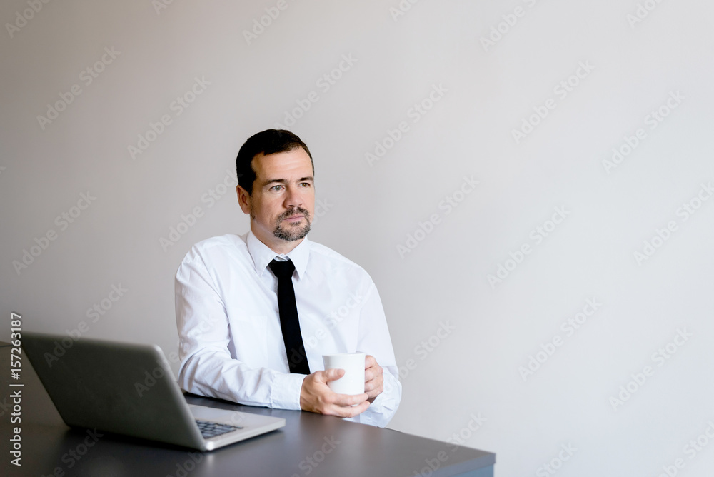 Pensive senior businessman sitting in his office and drinking a cup of coffee while taking a break. Pensive senior businessman sitting in his office and drinking a cup of coffee while taking a break.