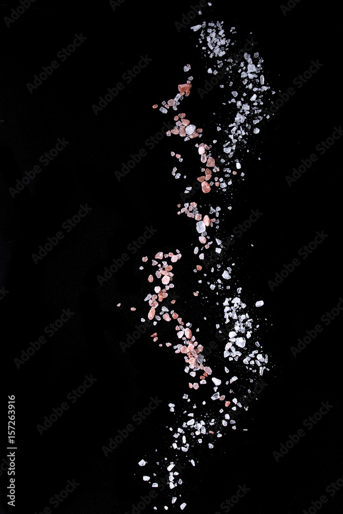 Obraz premium Sifting sea and pink Himalayan salt over black background. Isolated