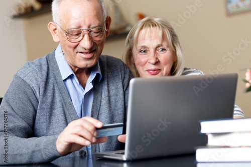 Senior couple, with laptop, shopping on line at home.