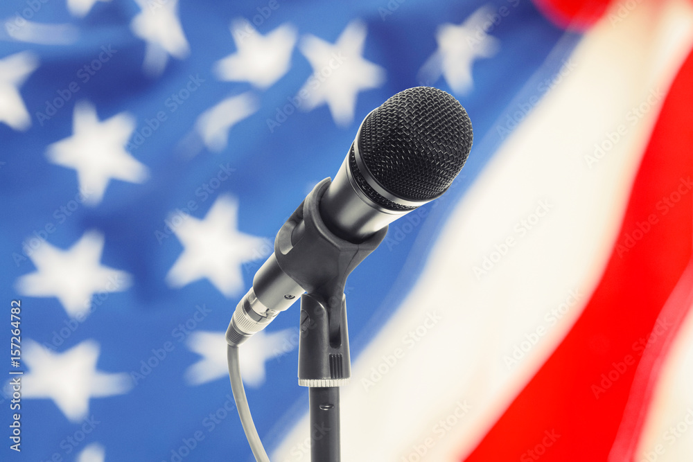 Microphone on stand with USA flag on background. Filtered image: cross processed vintage effect.