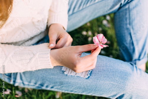 Female hands with neutral manicure holding an apple tree pink flower. Outdoors, spring.