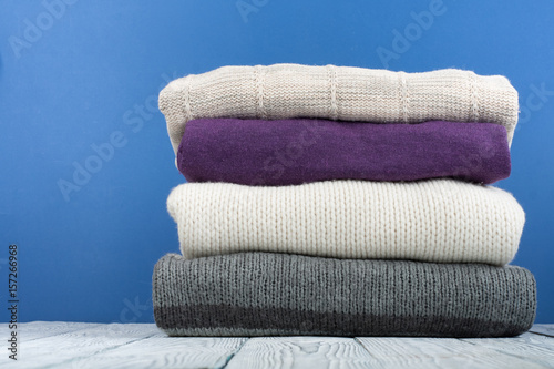Knitted wool sweaters. Pile of knitted winter, autumn clothes on blue, wooden background, sweaters, knitwear, space for text.
