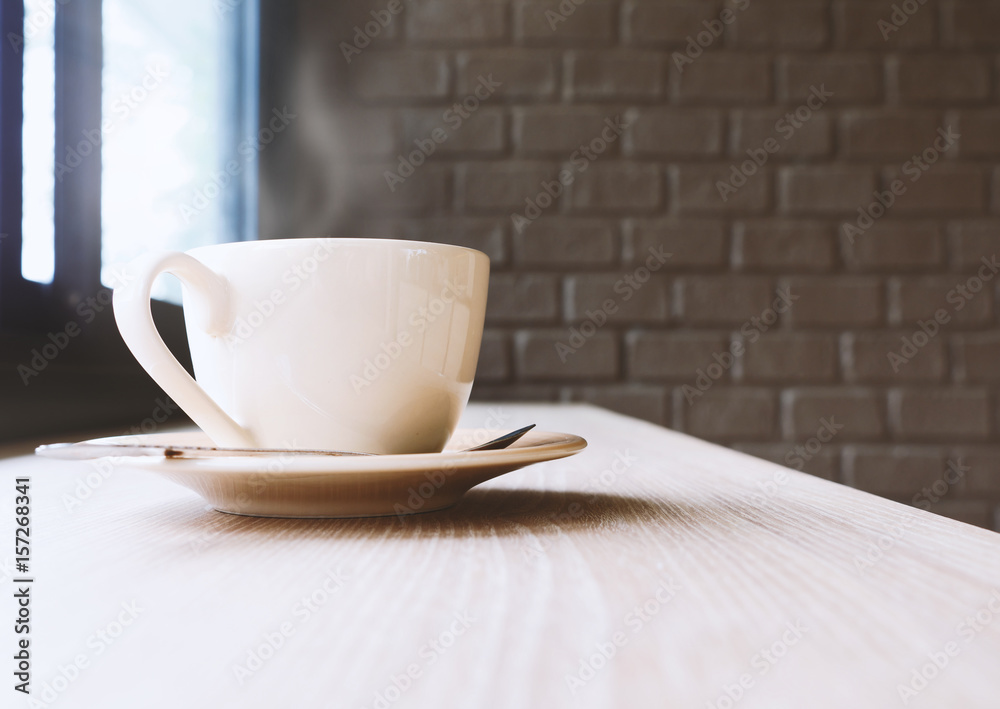 Coffee cup on wooden table against brick wall background with smoke and window lighting. Selective focus. Coffee cup on wooden table against brick wall background with smoke and window lighting. Selective focus.