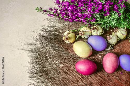 Brightly colored Easter eggs near the bouquet of wild flowers and dried buds of roses on a underlay of straw 

