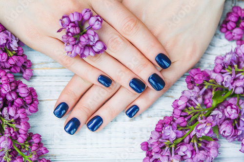 Beauty treatment, woman hands with dark blue manicure and beautiful fresh lilac flowers