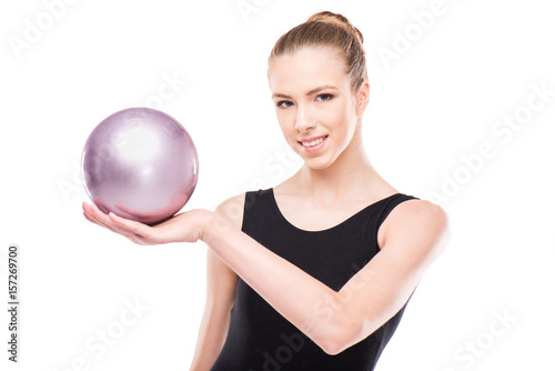 attractive rhythmic gymnast in bodysuit smiling, holding ball and looking at camera isolated on white