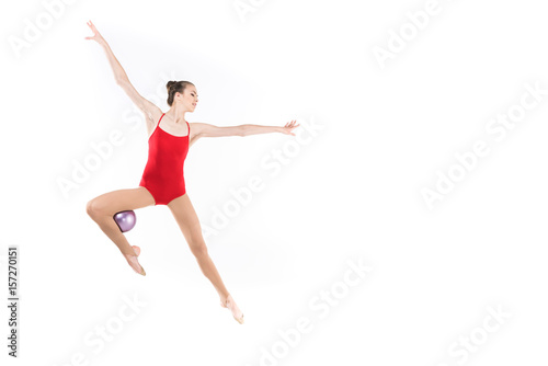 young caucasian woman rhythmic gymnast jumping with ball and looking away